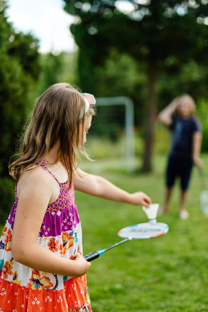 A young girl enjoys a sunny day playing badminton in a lush green park.